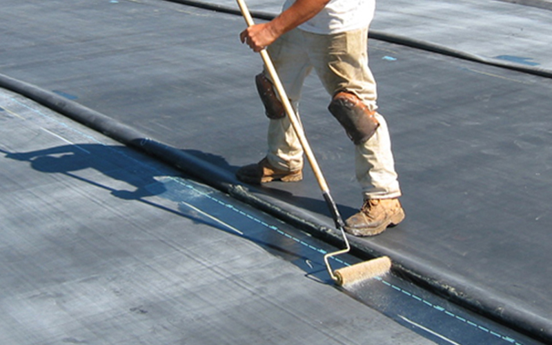 a commercial roofer wearing dirty jeans applies a flat roofing system