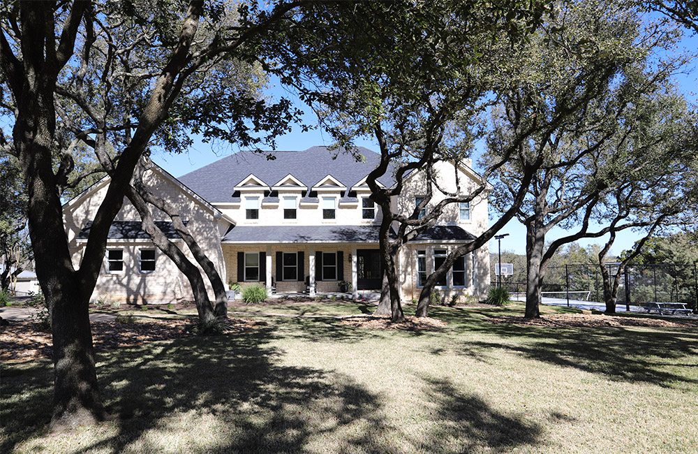 a classic home with many trees in austin texas that received a roof replacement with blue shingles