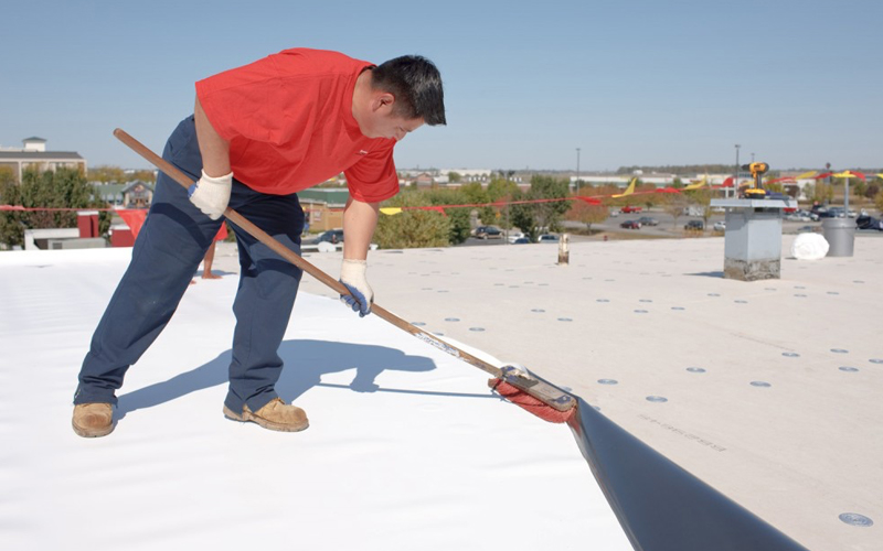 a roofer wearing a red t-shirt applies a tpo roof system to a commercial business